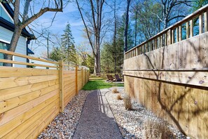 A wooden fence, gravel path, and a grassy area with trees and a building in the background. - Dartwood Dunes, Dunes, Lakes, Union Pier, Hot Tub (Union Pier)