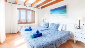 A bedroom with a large bed, two bedside tables, a window with curtains, and a painting on the wall. - Mallorca Finca with Pool Directly on the Sea Es Trenc (Sa Ràpita)