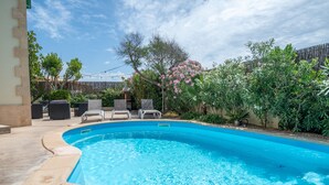 A swimming pool with a curved edge, surrounded by a patio area with lounge chairs and a wooden fence. - Mallorca Finca with Pool Directly on the Sea Es Trenc (Sa Ràpita)