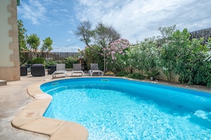 A swimming pool with a curved edge, surrounded by a patio area with lounge chairs and a wooden fence.