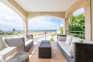 A covered outdoor seating area with wicker furniture, a view of the sea, and a paved pathway. - Mallorca Finca with Pool Directly on the Sea Es Trenc (Sa Ràpita)