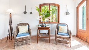 A room with two wicker chairs, a small wooden table, a floor lamp, and a window with a view of greenery. - Mallorca Finca with Pool Directly on the Sea Es Trenc (Sa Ràpita)
