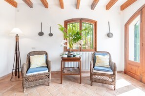 Una habitación con dos sillones de mimbre, una mesita de madera, una lámpara de pie y un ventanal con vistas a follaje.