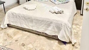 Un letto rifatto con cuscini e asciugamani, una testiera e un armadio con finitura in legno chiaro.