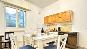 Una cucina moderna con mobili bianchi, un tavolo da pranzo con sedie imbottite blu e vista sugli alberi dalla finestra.