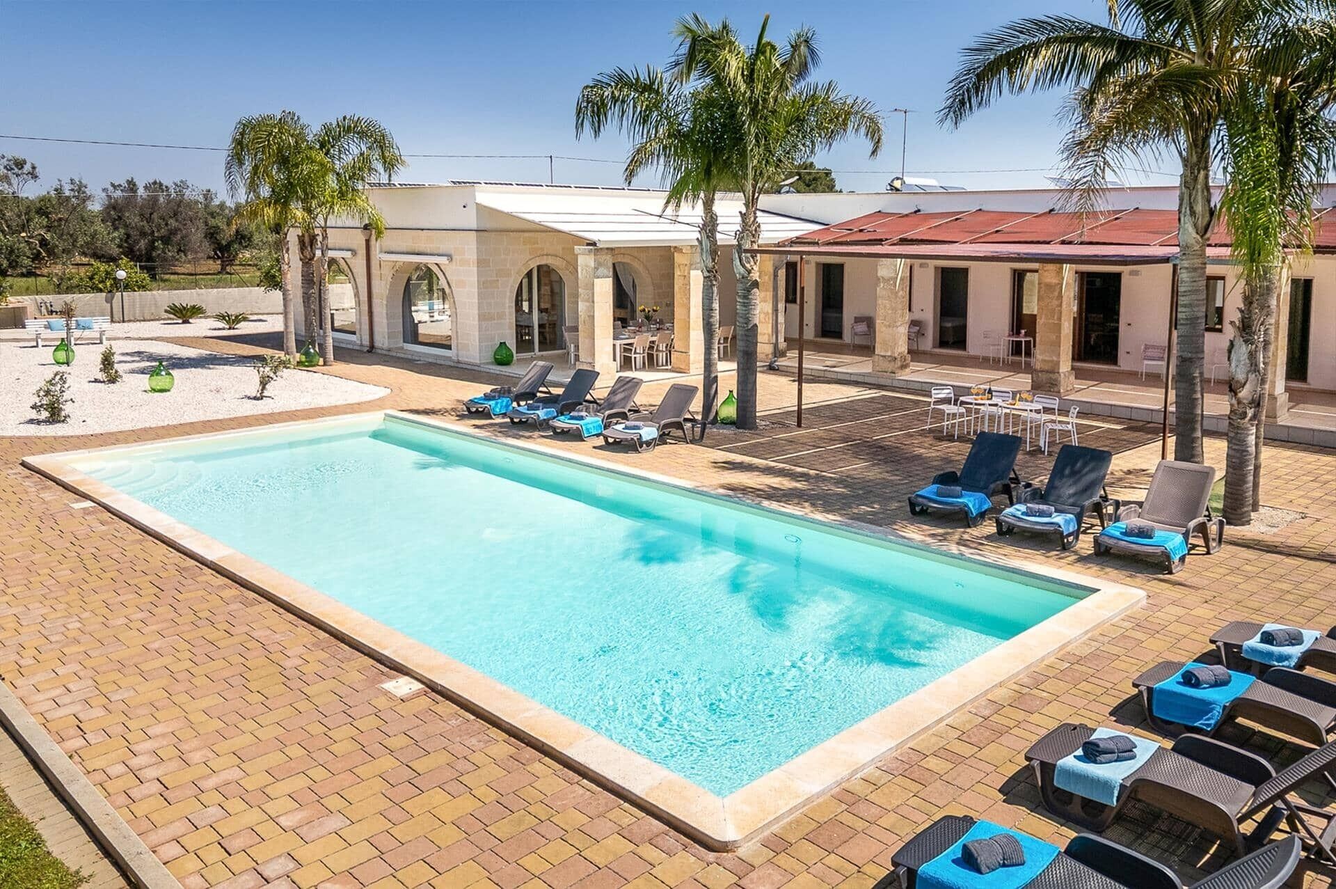 A swimming pool with lounge chairs and palm trees.