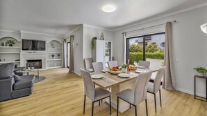 Un salon moderne avec une cheminée, un coin repas avec une table et des chaises en bois, et une grande fenêtre donnant sur un paysage verdoyant.