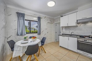 Eine kleine Küche mit weißen Schränken, einem eingebauten Backofen und einer Essecke mit Tisch für zwei Personen.