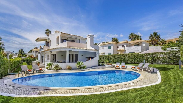 Une villa moderne dotée d’une piscine, de chaises longues et d’un jardin bien entretenu.