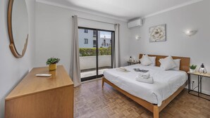 Une chambre d’hôtel avec un lit, un bureau, une plante en pot, un grand miroir et une porte-fenêtre coulissante donnant sur un balcon.