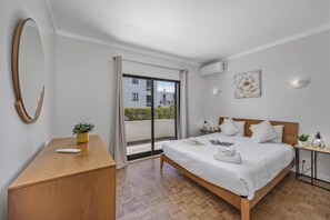 Ein Hotelzimmer mit einem Bett, einem Schreibtisch, einer Topfpflanze, einem großen Spiegel und einer Glastür zum Balkon.