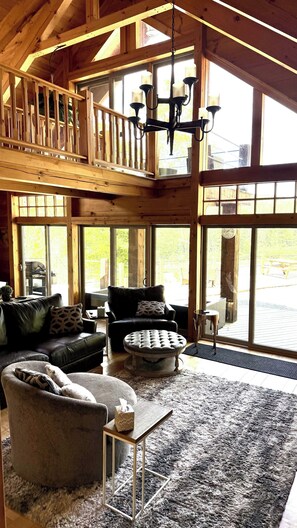 A spacious living area with a high ceiling, large windows, and a chandelier.