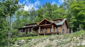 Eine Holzhütte mit Veranda, umgeben von Bäumen und einem felsigen Hang.