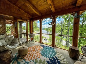 A cozy room with a large window, a woven chair, a round table, and a patterned rug.