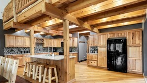 Eine Küche mit Holzschränken, einem schwarzen Kühlschrank und einer Holzeile mit Hocker.
