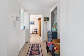 Un couloir avec un tapis Ă motifs, un lit recouvert dâune couverture colorĂ©e et une commode bleue.