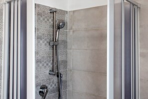 Une douche Ă©quipĂ©e dâun pommeau de douche Ă main et dâun pommeau de douche fixe fixĂ© au mur, tous deux dotĂ©s de finitions chromĂ©es.