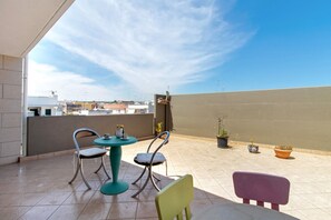 Eine Dachterrasse mit Tisch und Stühlen, Blumentöpfen und Blick auf die Stadtlandschaft.