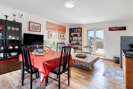 A dining area with a table set for four, a bookshelf, a television, and a window with a view.. Apartment 'La Mansarda - Terrazze Relax A Due' with Balcony, Wi-Fi and Air Conditioning