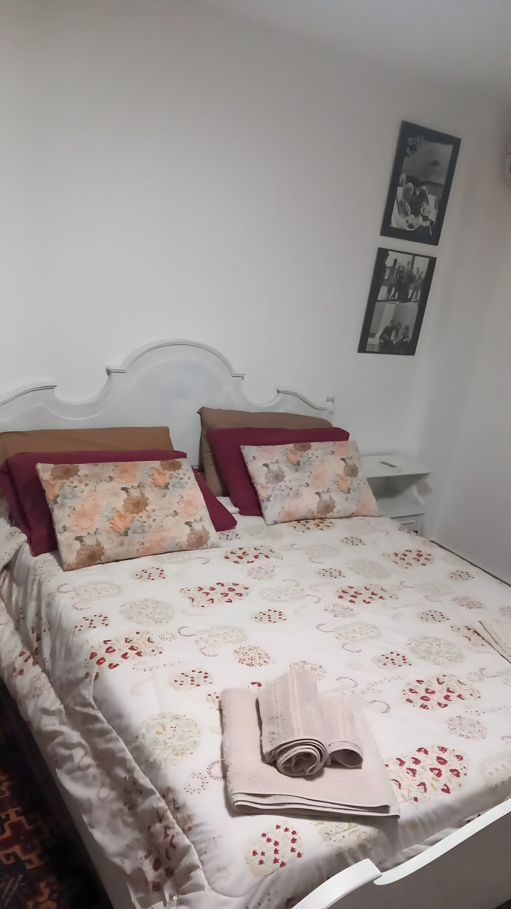 A neatly made bed with floral bedding, a headboard, and a nightstand with a lamp.