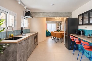 Eine moderne Küche mit einer zentralen Kochinsel, einem Essbereich mit orangefarbenen Stühlen und einer Bar mit blauen Stühlen.