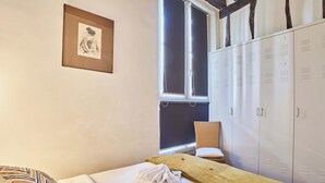 Een slaapkamer met een bed, een houten bankje, een raam, een stoel en een garderobe.