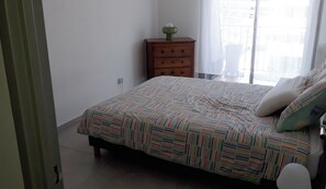 A bedroom with a bed, a nightstand, a wall socket, and a window with curtains. - Beautiful apartment with shared pool in Vallauris (Vallauris)