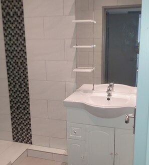 A bathroom with a white sink, a mirror, and a door. There are white cabinets and a tiled wall. - Beautiful apartment with shared pool in Vallauris (Vallauris)