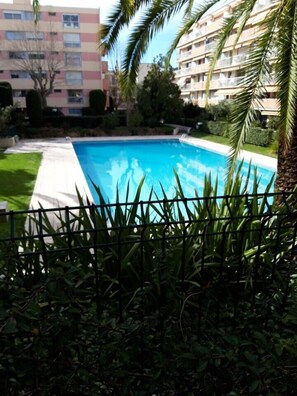 A swimming pool surrounded by greenery and a fence, with buildings in the background. - Beautiful apartment with shared pool in Vallauris (Vallauris)