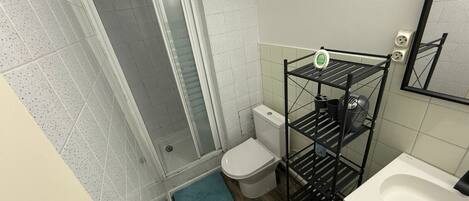 A bathroom with a shower, toilet, sink, and a metal shelf unit.