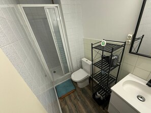 Ein Badezimmer mit Dusche, Toilette, Waschbecken und einem Regalschrank.