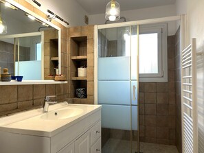 Ein Badezimmer mit Waschbecken, Spiegel, Regalen mit Körben und einer Duschkabine aus Glas.