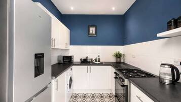 A compact kitchen with a washing machine, microwave, stove, and a coffee maker.