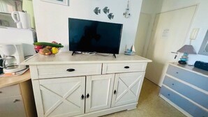 Une petite cuisine équipée d’une télévision, d’une machine à café et d’un panier de fruits posé sur le comptoir.