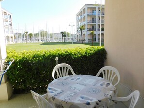 Ein Balkon mit Tisch und Stühlen, der auf eine gepflegte Rasenfläche und ein Gebäude mit Balkonen blickt.