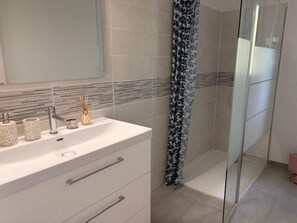 A modern bathroom with a white vanity, a glass shower enclosure, and a patterned shower curtain. - Seaside apartment with terrace and parking (Aytré)