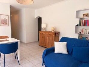 A living room with a blue sofa, a wooden cabinet, a white table, and a bookshelf. - Seaside apartment with terrace and parking (Aytré)