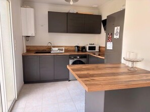 A compact kitchen with grey cabinets, a wooden countertop, a washing machine, and a microwave. - Seaside apartment with terrace and parking (Aytré)