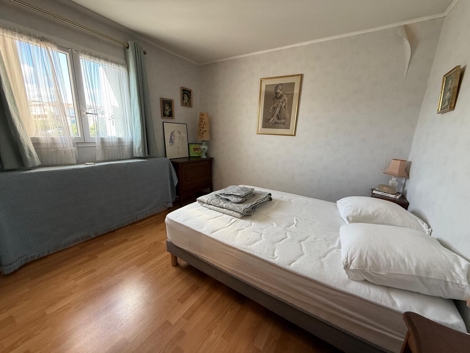 A bedroom with a bed, a nightstand, a window with curtains, and wall-mounted pictures.