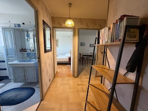 A hallway with a wooden floor, a kitchen with a sink and cabinets, a dining area with a table and chairs, and a bookshelf with books. - Apartment with balcony and parking Cagnes-sur-Mer (Cagnes-sur-Mer)