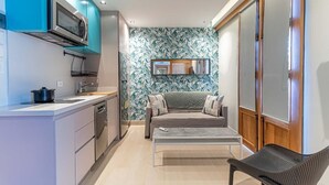Una cocina compacta con microondas, estufa y lavaplatos, un sofá con cojines, una mesita y una silla.