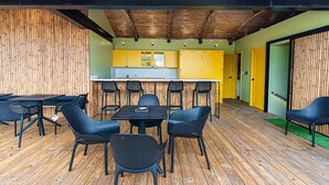 A covered outdoor dining area with tables and chairs, a kitchen in the background, and a bamboo wall. - RooftopTerrace·ZonaColonial·Cathedral|YELLOWKEY (Santo Domingo)