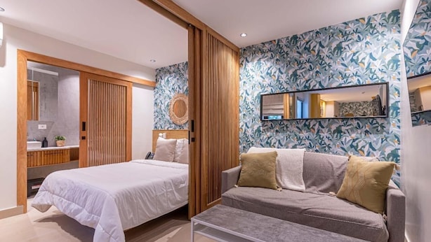 Una habitación de hotel moderna con una cama, un sofá, una mesa de centro, un espejo y una pared con diseño.