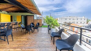 Terraza de madera con asientos al aire libre, una planta en maceta y vistas de la ciudad.