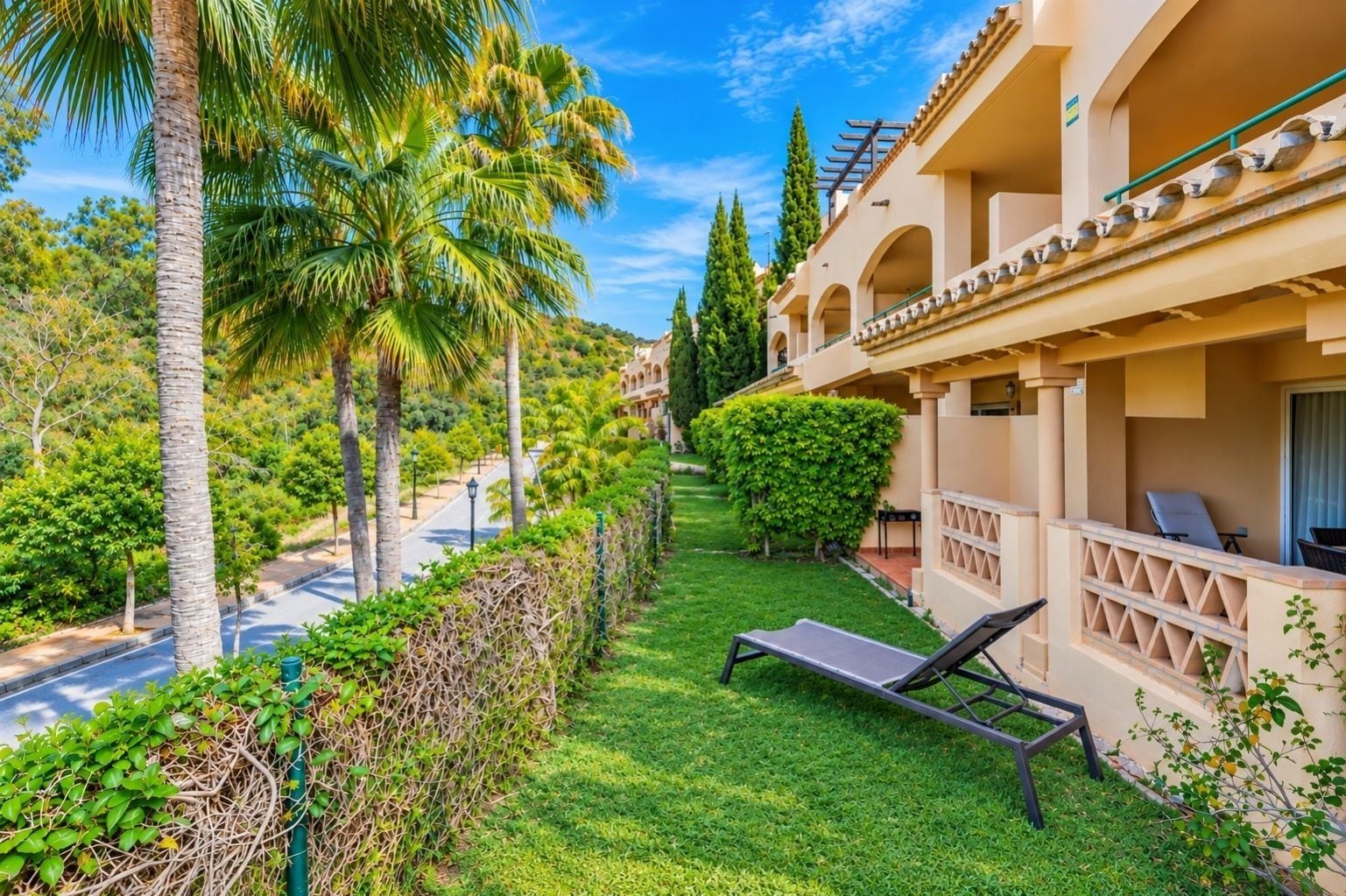 Un balcon d’hôtel avec un fauteuil de relaxation, une pelouse bien entretenue et une vue dégagée sur la rue.