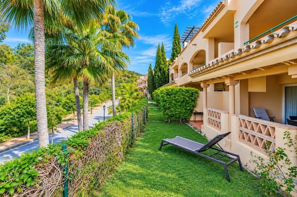 A hotel balcony with a lounge chair, a well-maintained lawn, and a clear view of the street. - GuestReady - Peaceful retreat with pool (Marbella)