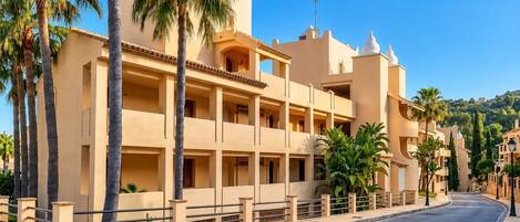 A multi-story hotel with balconies, palm trees, and a clear sky.