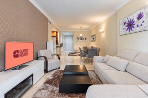 A modern living room with a flat-screen TV displaying 'GUEST READY,' a dining area with a table and chairs, and a hallway leading to a kitchen. - GuestReady - Peaceful retreat with pool (Marbella)
