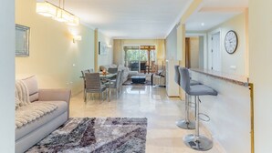 A modern living room with a sofa, a dining table, and two bar stools. - GuestReady - Santa Maria Village (Marbella)