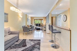 A modern living room with a sofa, dining table, chairs, and a kitchen area with a bar. - GuestReady - Peaceful retreat with pool (Marbella)